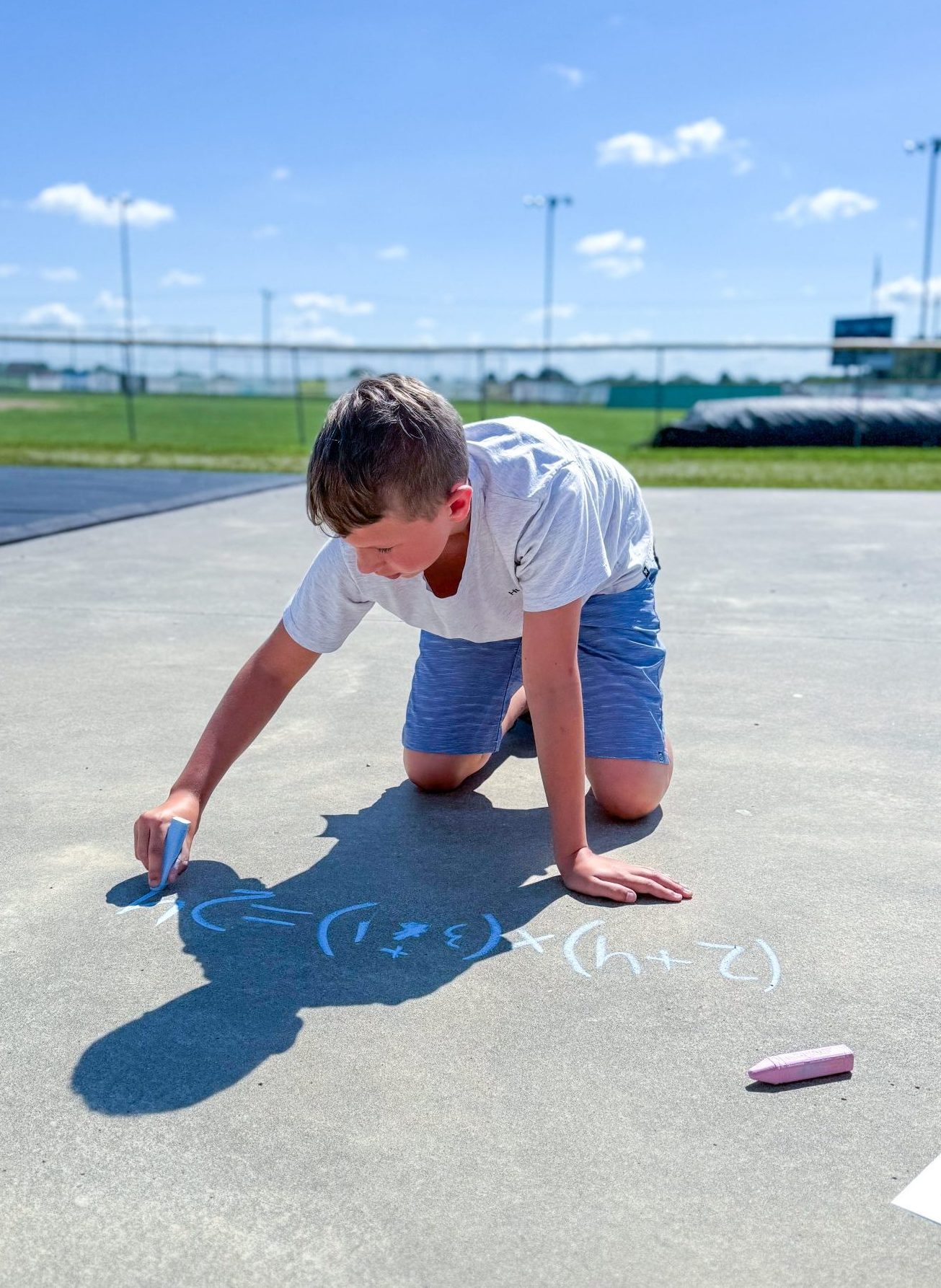 Student writing a math equation outside with sidewalk chalk