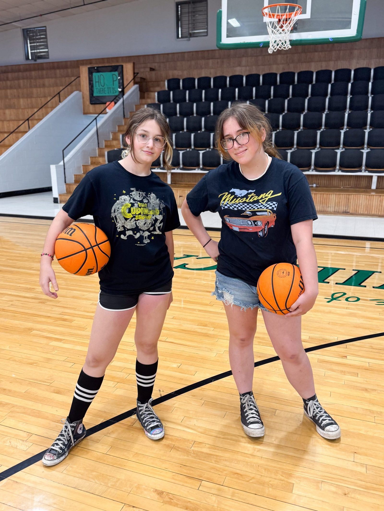 Two students posing with basketballs in a gym